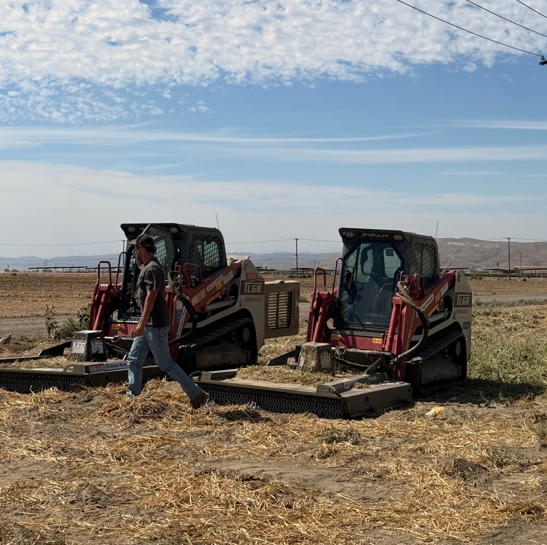 Two skid steers with heavy-duty brush mower attachments on a cleared job site.